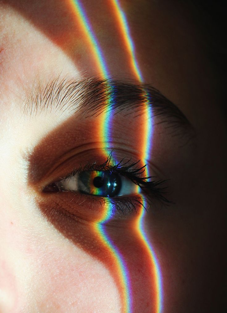 a woman's eye with rainbow colored lines on the outside of her face and part of her body visible