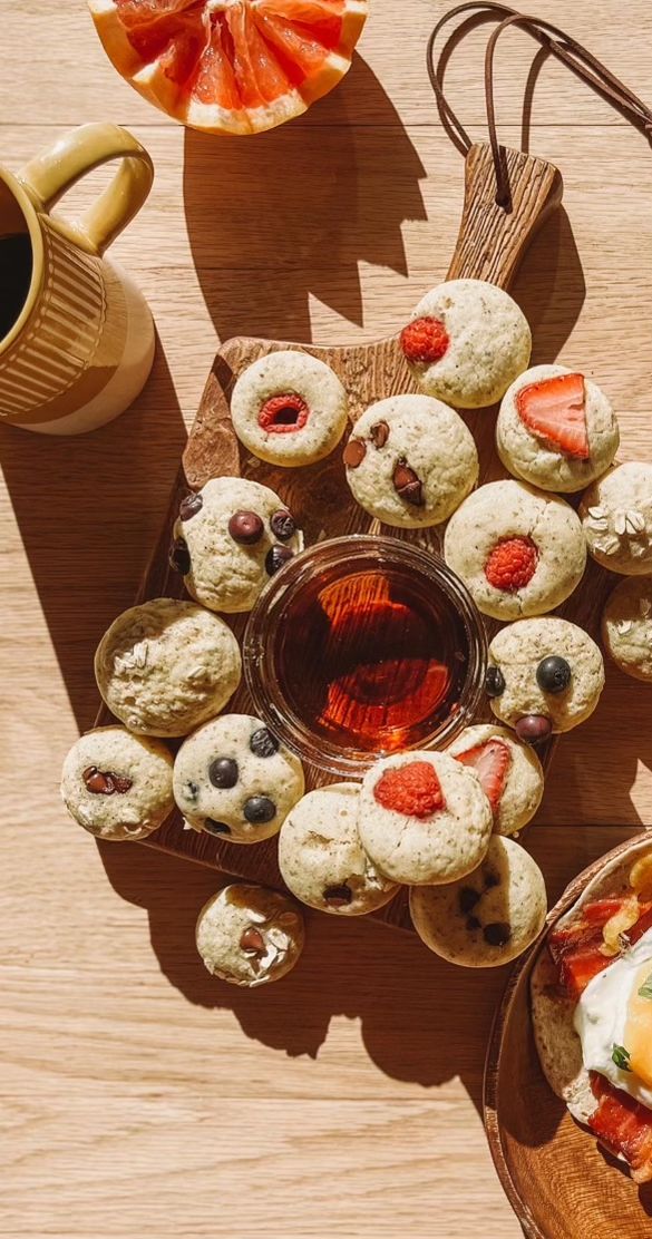 a table topped with pastries and fruit next to a cup of coffee on top of a wooden table