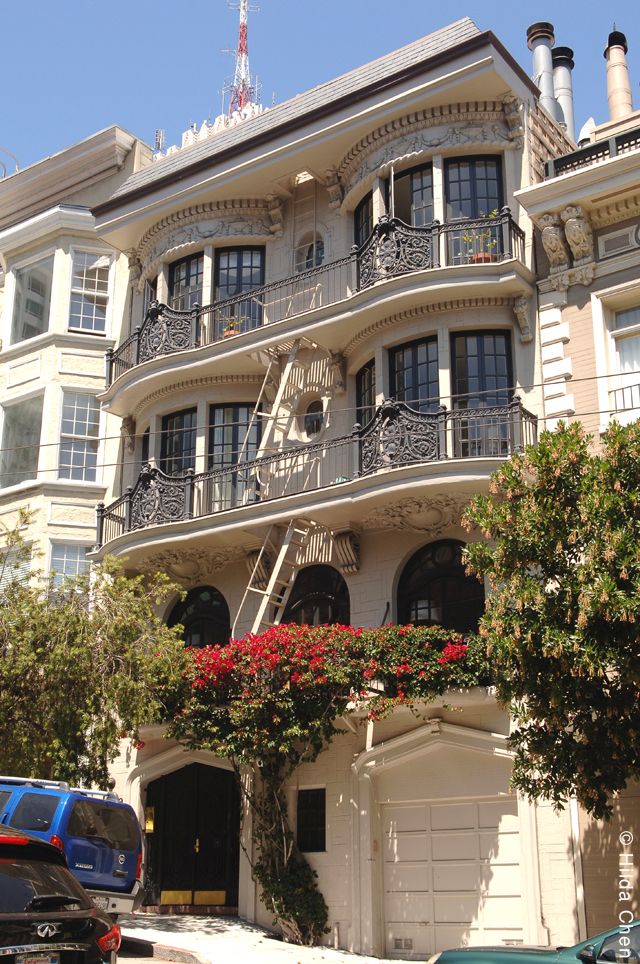 a large white building with many balconies and flowers on the balcony, next to a blue car