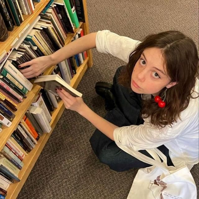 a woman sitting on the floor in front of a bookshelf holding a book