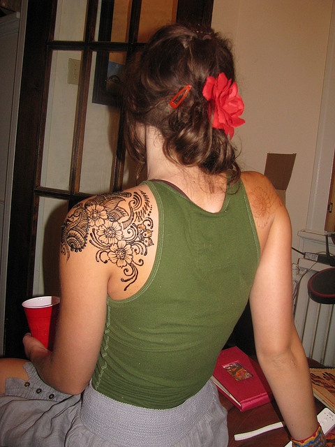 a woman with a red flower in her hair and tattoos on her back, sitting at a table