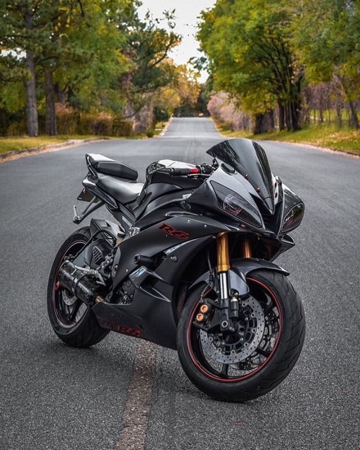 a black motorcycle parked on the side of a road next to some trees and grass