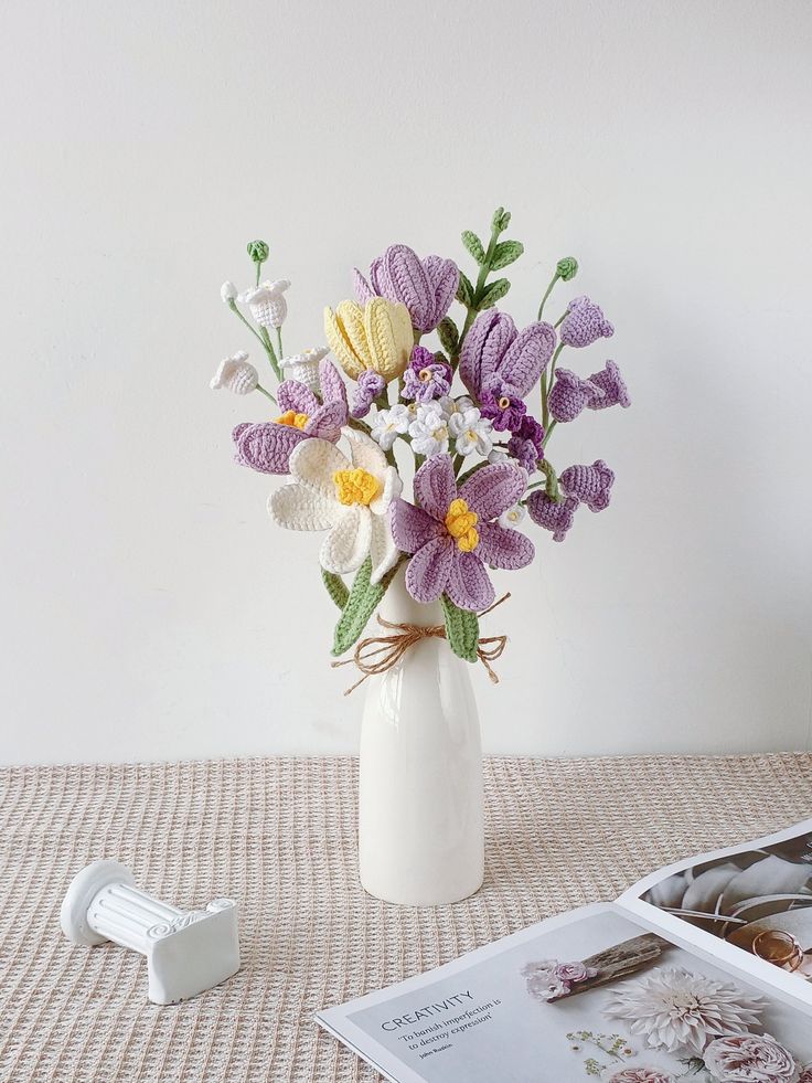 a vase filled with purple and white flowers on top of a table next to a magazine