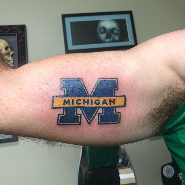 a man's arm with a michigan tattoo on it and a skull in the background