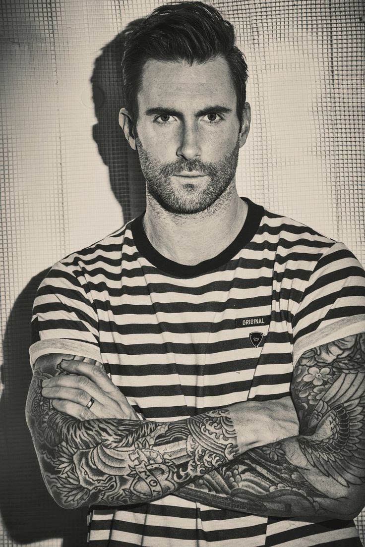 a man with tattoos standing in front of a wall