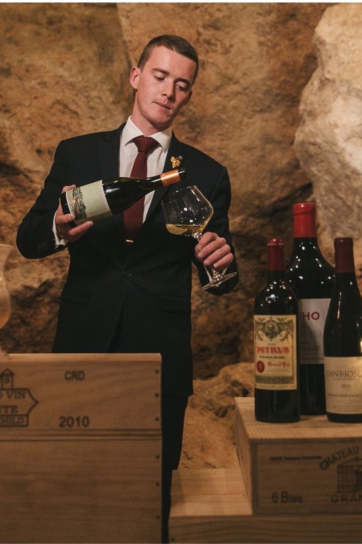 a man in a suit and tie holding a glass of wine next to some bottles