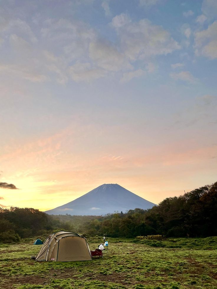 there is a tent set up in the field with mountains in the background at sunset