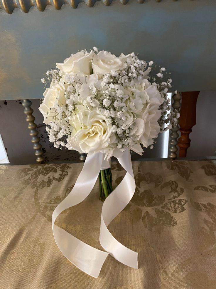 a bridal bouquet with white flowers and ribbon on a tableclothed surface in front of a mirror