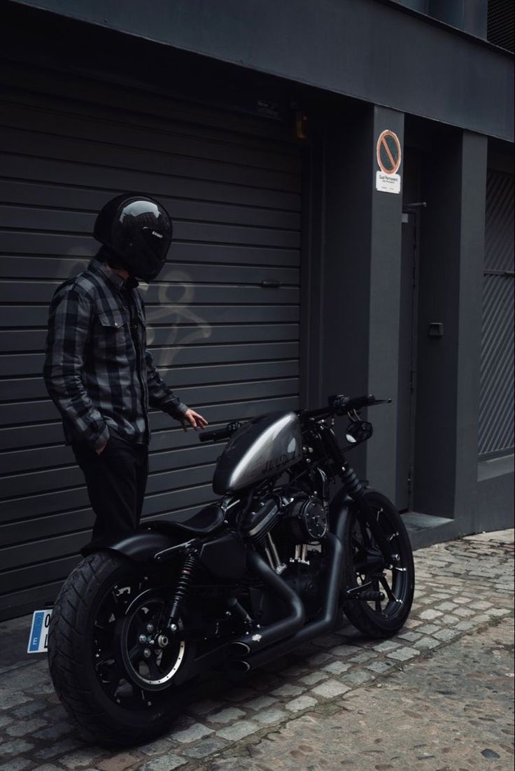 a man standing next to a parked motorcycle on a brick road in front of a garage door