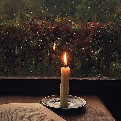 a lit candle sitting on top of a table next to an open book and window