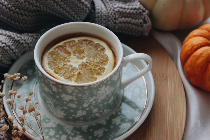 a cup of tea with a slice of orange in it on a saucer next to some pumpkins