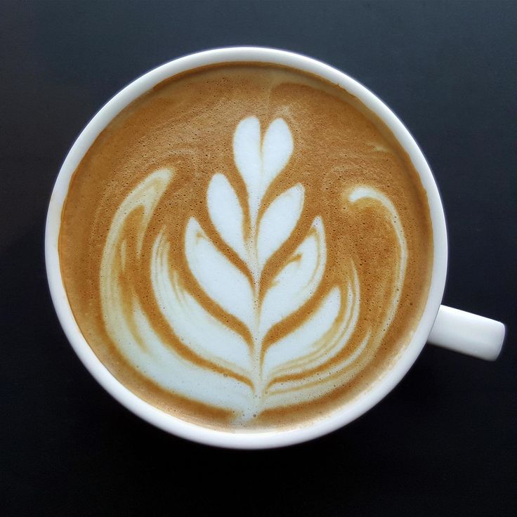 a cappuccino in a white cup on a black table with a leaf design