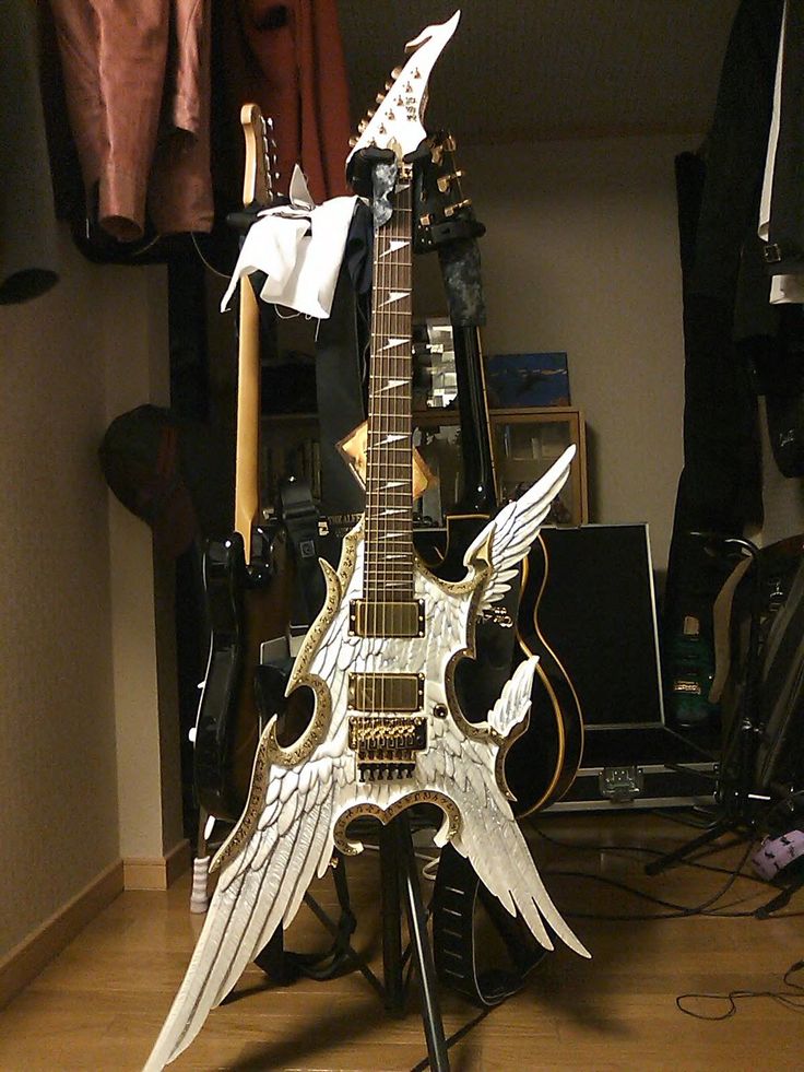 an electric guitar with wings on it sitting in front of a rack full of guitars