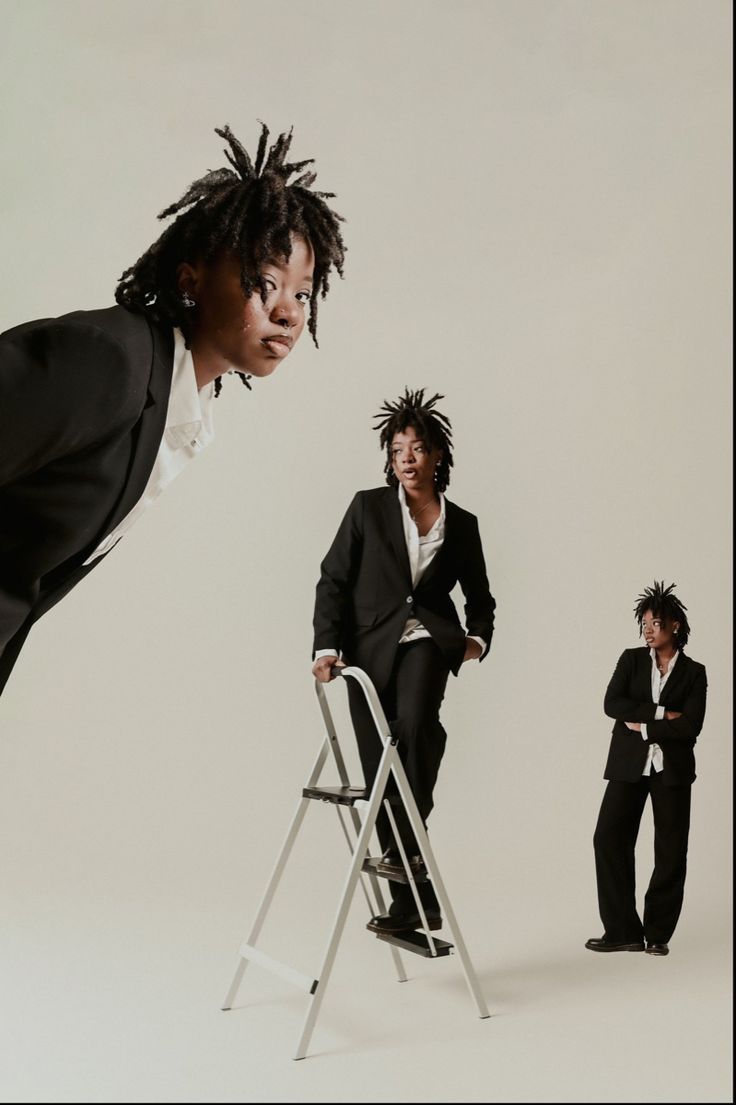 two women in suits and one is standing on a ladder with her hair blowing back