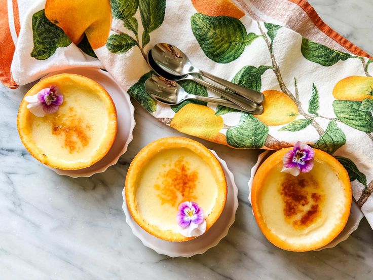 three small desserts with flowers on them are sitting on a marble counter top next to utensils