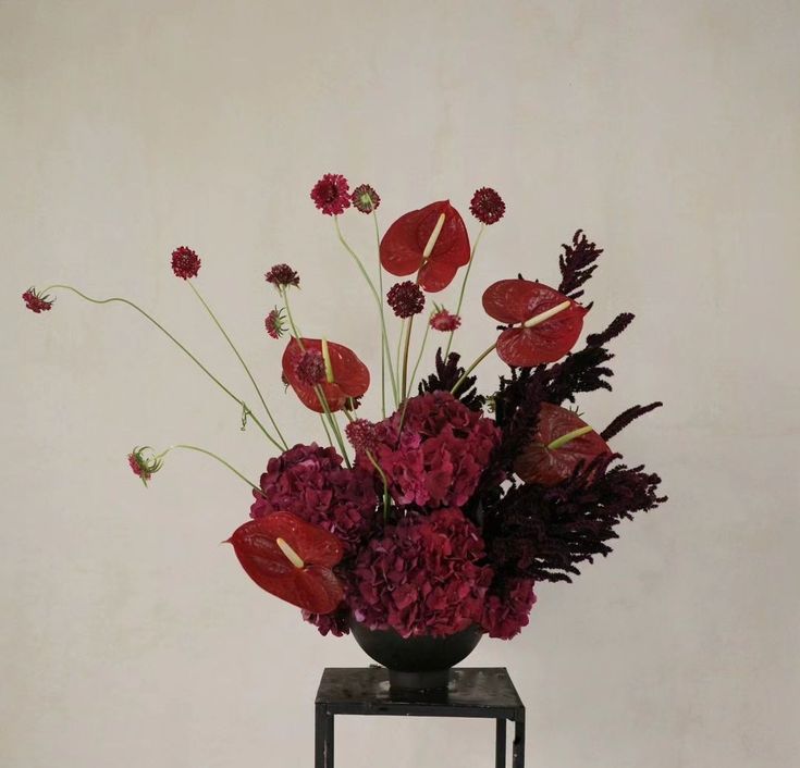 a vase filled with red flowers on top of a wooden table next to a white wall