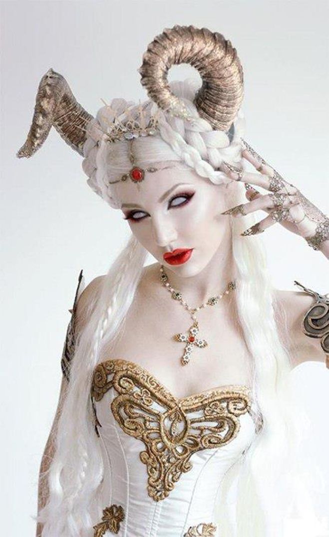 a woman dressed in white and gold with horns on her head