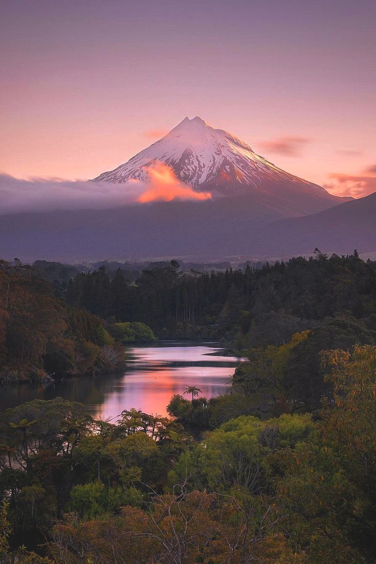 the sun is setting over a mountain with trees in front of it and a body of water below