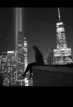 a woman sitting on top of a building looking at the city lights in black and white