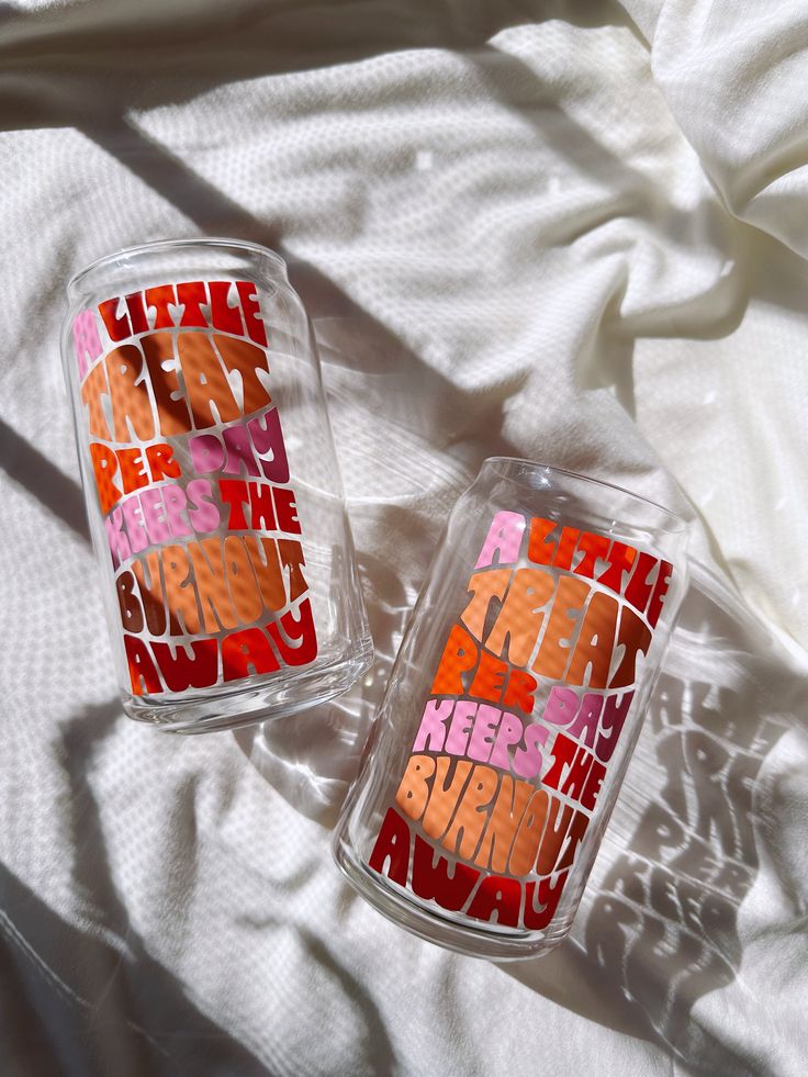 two tumblers sitting on top of a bed covered in white sheets and colorful lettering