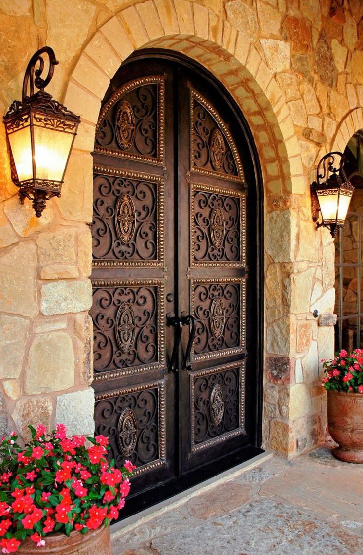 an entrance to a home with two large doors and flowers in the planters outside