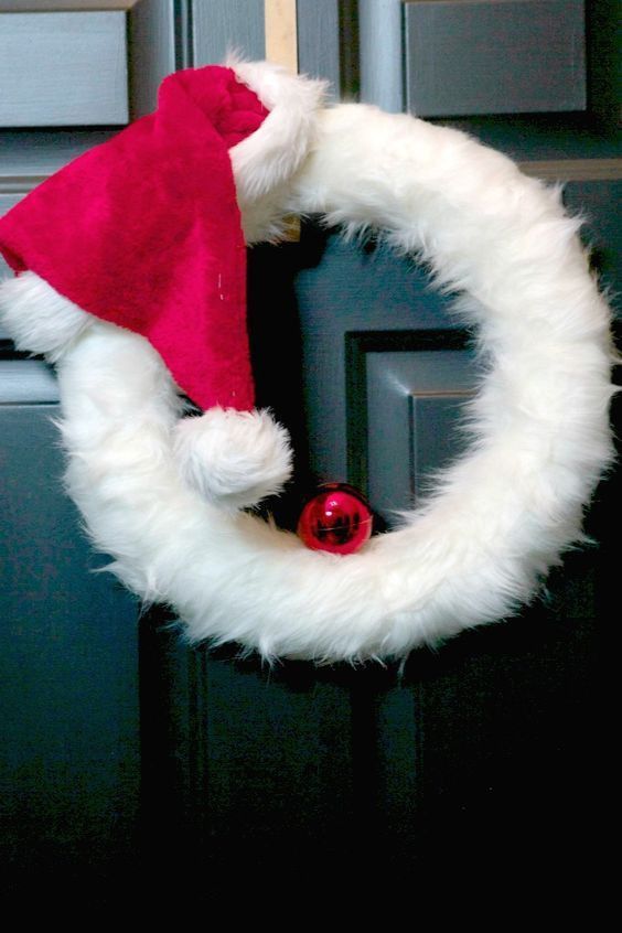 a white wreath with a red santa hat hanging on the front door to give it a festive touch