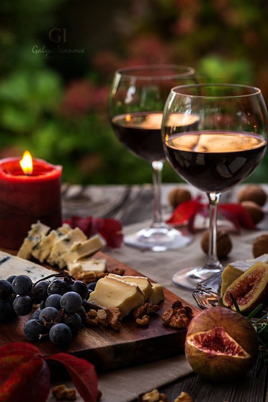 two glasses of wine and cheese on a table with grapes, figs and nuts