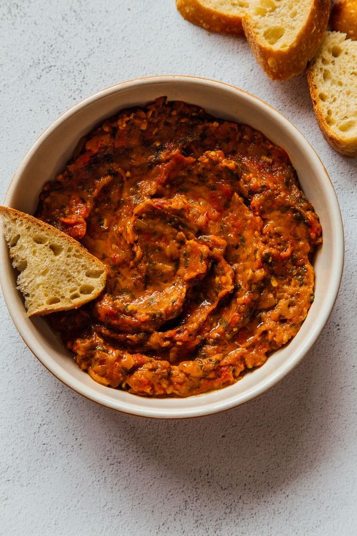 a white bowl filled with food next to slices of bread on top of a table