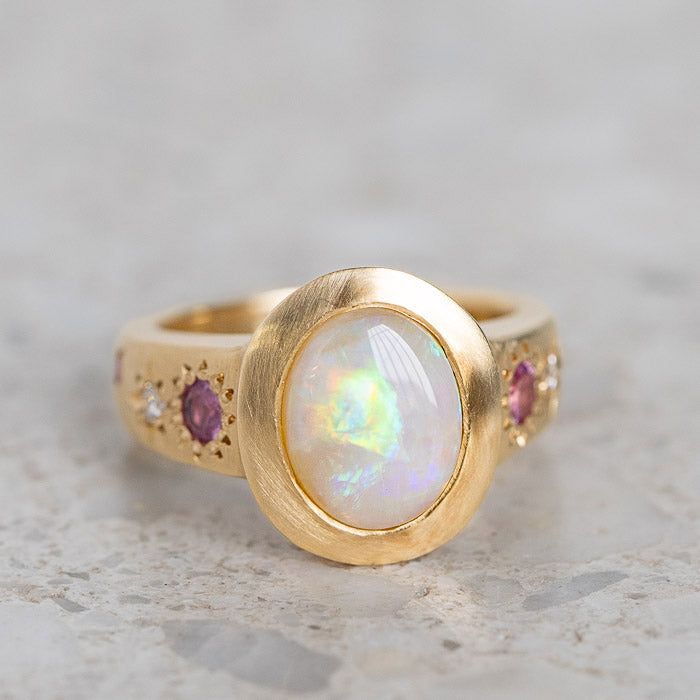 Our Sun Punch Ring has been set with a Crystal Opal from Coober Pedy and bead set with Pink Sapphires, G/VS White Diamonds and Salt & Pepper Diamonds in the band. Opal measures approx. 10 x 8mm. There are a total of three birlliant cut pink sapphires and four brilliant cut diamonds. Band width tapers from approx. 6mm to 3.4mm at the back of the band. Gold weight approx. 11g in 14ct, 12.6g in 18ct. This ring is pictured with a matte finish. For a polished finish please leave a note at the checkout. Please note, we will match the opal as close to the image as possible. Each opal is unique and may vary in appearance and colour from what is depicted on the site. Unconventional Engagement Rings, Opal Wedding Ring, Coober Pedy, Crystal Opal, Bead Set, Jewelry Lookbook, Salt And Pepper Diamond, Opal Ring, Opal Crystal