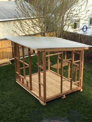 a small wooden structure sitting in the grass next to a tree and fenced yard