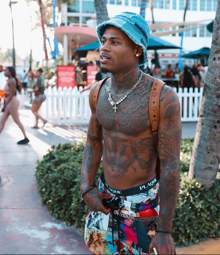 a man with tattoos on his chest wearing shorts and a blue bandana is walking down the street