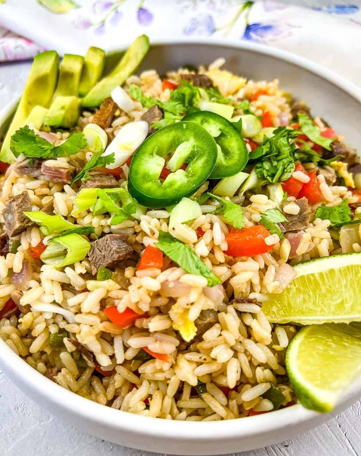 a white bowl filled with rice and veggies next to sliced limes on the side