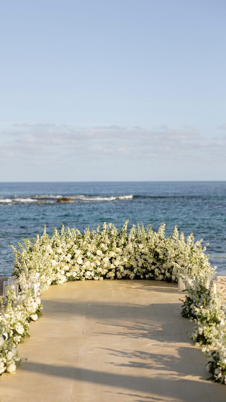 an outdoor wedding ceremony setup with flowers and candles on the aisle, overlooking the ocean