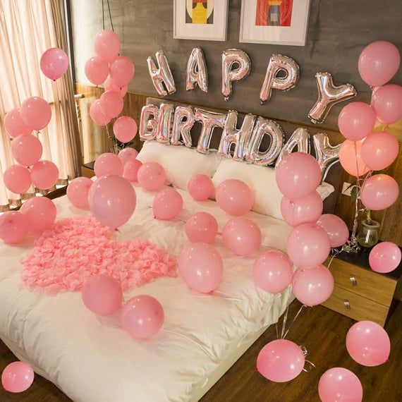 a bedroom decorated with balloons and pink confetti on the bed for a birthday party