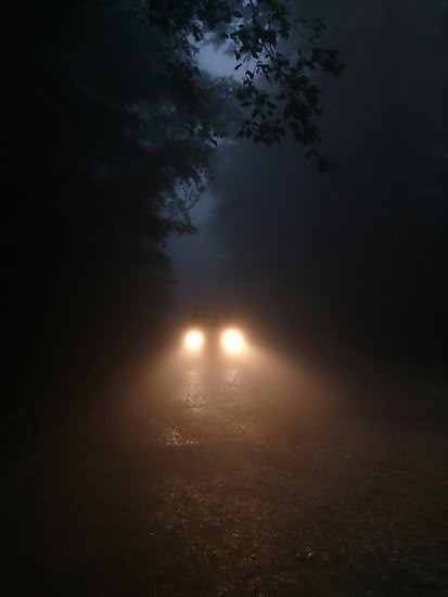 two cars driving in the dark on a foggy road at night with headlights up