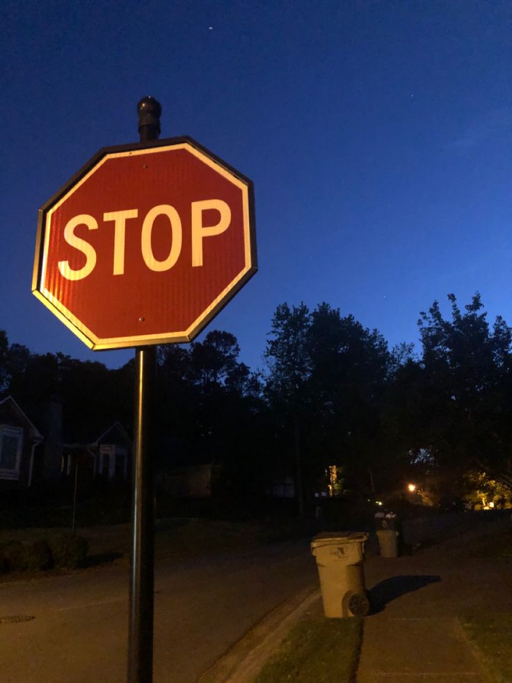 a red stop sign sitting on the side of a road next to a trash can