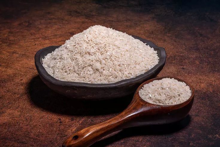 white rice in a wooden bowl and spoon on a brown surface with a dark background