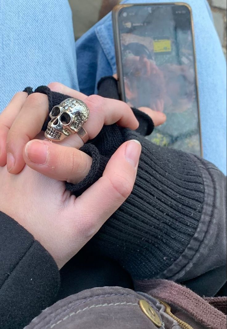 a person holding a cell phone with a skull ring on their finger and wearing gloves