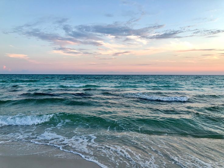 the ocean waves are coming in to shore at sunset or dawn, with pink and blue sky above