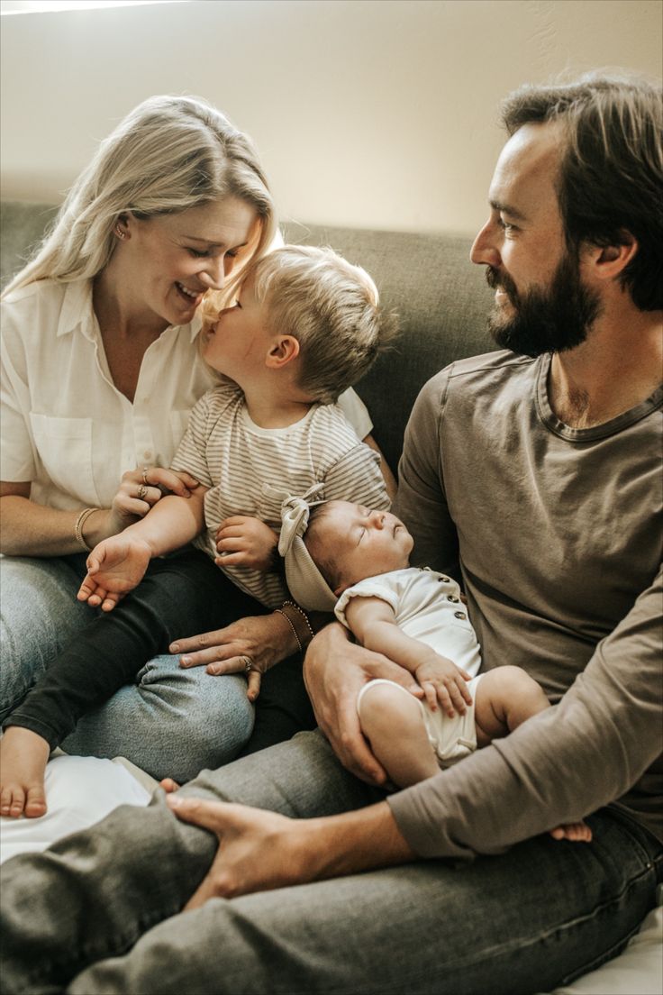 a man and woman sitting on a couch with two babys in their lap as they look at each other