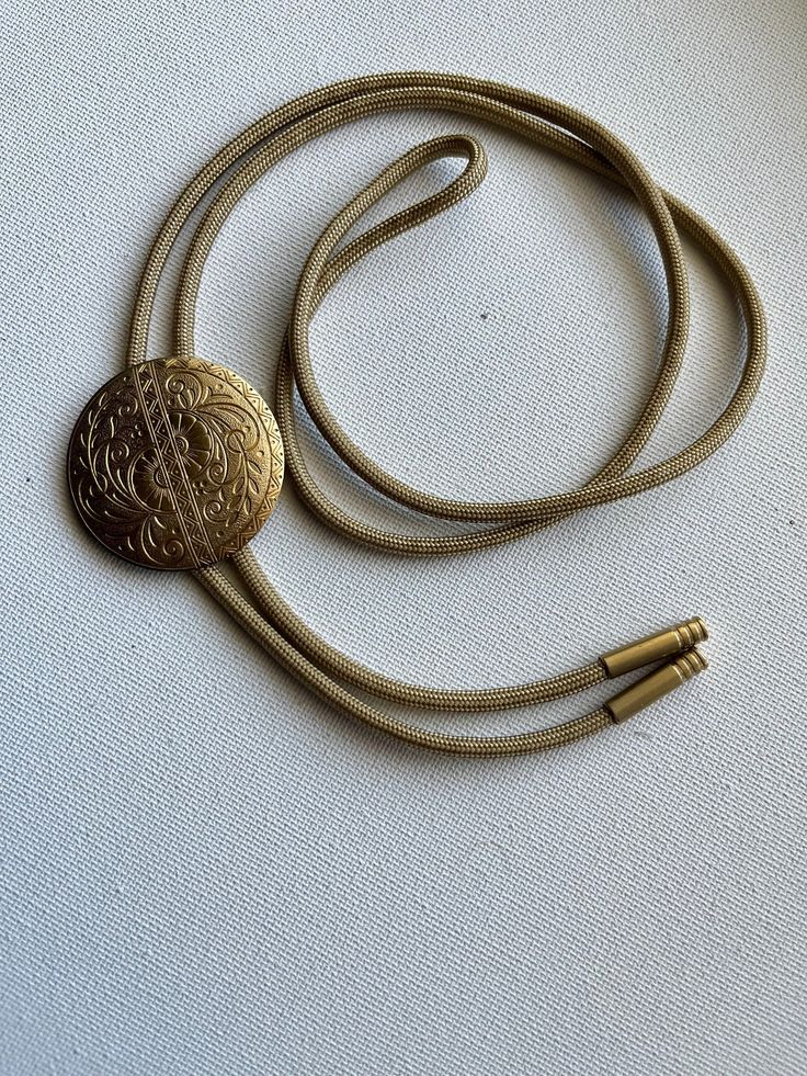 Brass floral medallion bolo tie necklace on light gold colored nylon cord. Gold Bolo Tie, Elegant Lariat Jewelry With Adjustable Cord, Elegant Adjustable Round Medallion Necklace, Elegant Round Medallion Necklace, Handmade Adjustable Medallion Necklace, Adjustable Brass Medallion Necklace, Antique Adjustable Yellow Gold Jewelry, Vintage Necklaces With Adjustable Length For Festivals, Vintage Lariat Jewelry With Sliding Knot