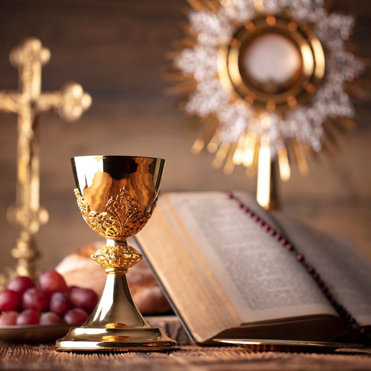 a golden chalice sitting on top of a table next to grapes and an open book