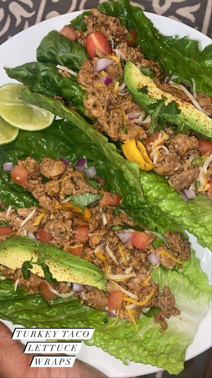 two lettuce wraps filled with meat and vegetables on a white plate next to lime wedges