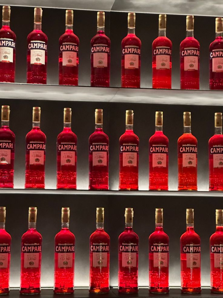 several bottles of red liquid are lined up on shelves