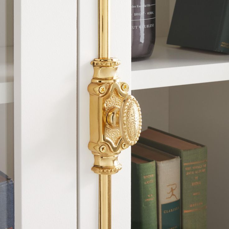 a gold door handle on the side of a white bookcase with books behind it