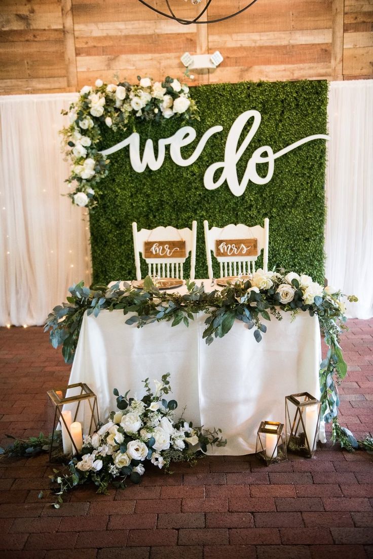 the table is set up with white chairs and greenery