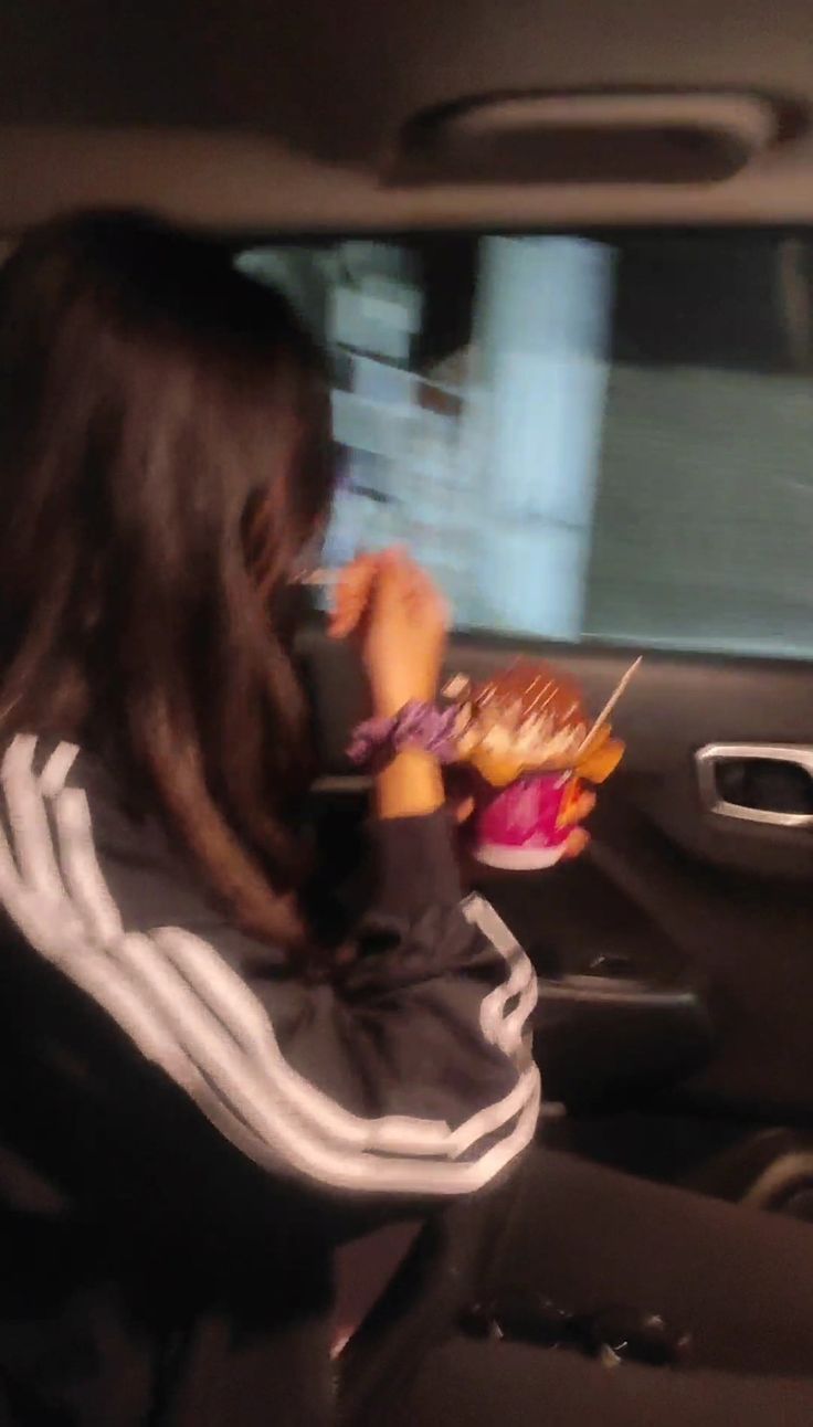 a woman sitting in the back seat of a car while eating food from a plate