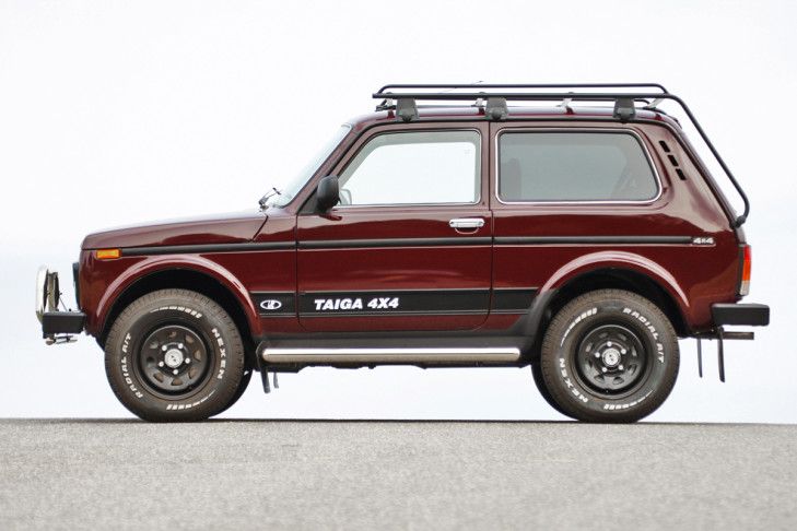 a red four door suv parked on top of a parking lot next to a white wall