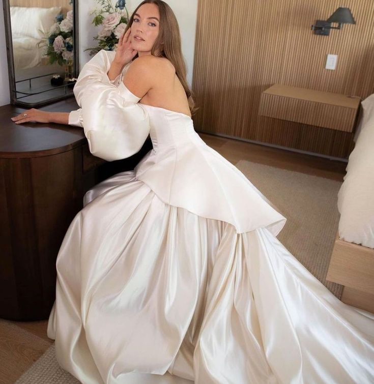 a woman in a white wedding dress sitting on a chair next to a dresser and mirror