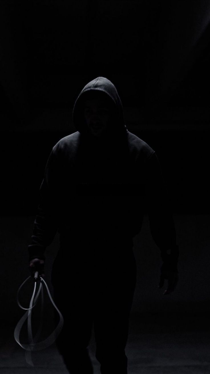 a person walking in the dark with a bag on his shoulder and a hoodie on